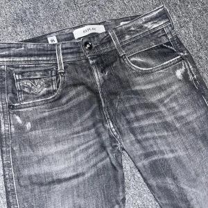 Replay anbass jeans  - Snygga mörkgråa Replay anbass jeans med coola slitningar och tvättad look. Klassisk femficksmodell med Replay-logga vid fickan. Jeansen har en rak passform och är tillverkade i mjukt denimtyg som sitter skönt hela dagen.