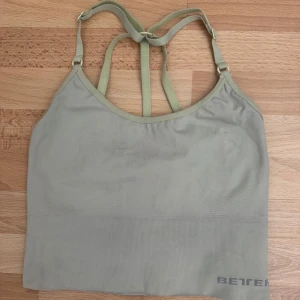 Grön linnetopp från Better Bodies - Säljer en ljusgrön linnetopp från Better Bodies med snygga dubbla axelband och brottarrygg. Toppen är sömlös och har en tight passform, perfekt för träning. Materialet är 92% polyamid och 8% elastan vilket gör den stretchig och bekväm. Utan bröstkuddarna.