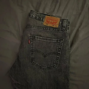 Levi's 502 svarta jeans W32 L32 - Säljer ett par gråa Levi's 502 jeans med klassisk femficksdesign och raka ben. Jeansen har en snygg tvättad look och är tillverkade i slitstarkt denim med den ikoniska läderpatchen bak i midjan.