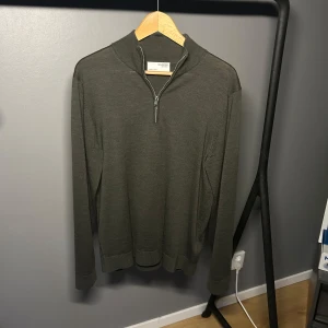 Mörkgrön half zip-tröja från Selected - Snygg mörkgrön långärmad tröja från Selected Homme med half zip-dragkedja i halsen. Tröjan är gjord i merinoull och har en stilren, enkel design som passar perfekt till lager-på-lager. Ribbade muddar vid ärmslut och nederkant. Har använt den kanske 3 gånger.