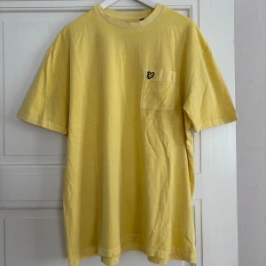 Gul boxy t-shirt från Lyle & Scott - Gul t-shirt från Lyle & Scott i boxy fit med bröstficka och broderad logga. Klassisk rund halsringning och korta ärmar. Tillverkad i mjuk bomull, perfekt för en chill och avslappnad stil.