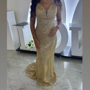 Glittrig guldig långklänning med paljetter - Säljer en superfin långklänning i guld med glittriga paljetter och broderade detaljer. Klänningen har en figurnära passform, sweetheart-urringning och medföljande avtagbara ärmar. Perfekt för bal eller fest där du vill sticka ut. Använd endast vid ett tillfälle finns inga tecken på användning storlek 36/38