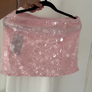 Rosa paljettkjol i kort modell - Supersöt rosa kortkjol täckt med glittriga paljetter. Kjolen har en rak passform och är perfekt för dig som vill sticka ut med en glammig look. Materialet är lätt och skimrande, vilket ger en extra festlig känsla.  Prislapp kvar som ny💕