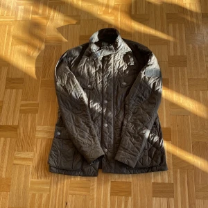 Quiltad brun Barbour jacka stl L - Säljer en brun quiltad jacka från Barbour i storlek L. Normal storlek. Värmer rätt bra till hösten. Väldigt lite använd och inga defekter vad jag kan hitta.