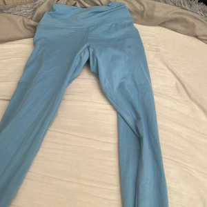 Blå leggings från Gymshark XS - Snygga ljusblå leggings från Gymshark i storlek XS. De har hög midja och är tillverkade i ett stretchigt material med 74% nylon och 26% elastan. Perfekta för träning och har en diskret logga baktill i midjan.