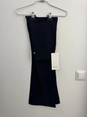 Svarta bootcut/flared leggings/tights från Lululemon storlek 6 - Svarta leggings från Lululemon i modellen Groove, tillverkade i supermjukt och stretchigt Nulu-material. Hög midja och bootcut-ben ger en snygg siluett. Perfekta för träning eller chill. Dold ficka i linningen och klassisk Lululemon-logga på benet.