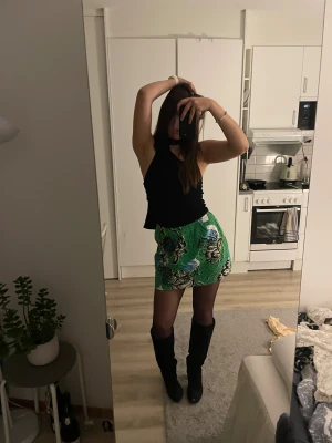 Mönstrad kjol - Säljer en färgstark grön kortkjol från River Island med stort blommigt mönster i svart, vitt, blått och gult. Kjolen har en rak form och synlig dragkedja bak. Materialet är strukturerat och känns som bomull. Perfekt för dig som gillar att sticka ut med coola prints.