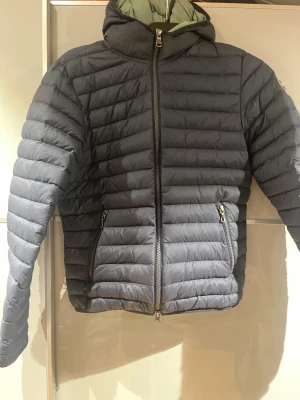 Mörkblå pufferjacka från Colmar - Säljer en mörkblå pufferjacka från Colmar med huva och två sidofickor med dragkedja. Jackan har quiltad design och hel dragkedja framtill. Perfekt för dig som vill ha en snygg och funktionell jacka till höst och vinter.