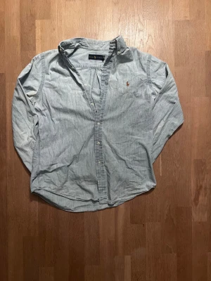 Ljusblå skjorta från Ralph Lauren - Klassisk ljusblå skjorta från Ralph Lauren med broderad logga på bröstet. Skjortan har lång ärm, knappar framtill och en avslappnad passform. Tillverkad i mjuk bomull, perfekt för en clean och stilren look. ✅   Passar för runt 184 🙌  8/10 skick endast lite bleknad i armhåla ✅ Skickar inom 48 timmar om inte samma dag 🚚