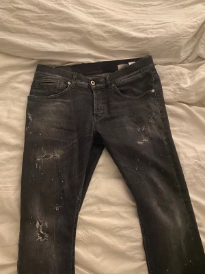 Svarta jeans med slitningar och stänk - Säljer ett par gråsvarta jeans från Dondup. Jeansen är skinny fit men skulle säga att de sitter mer som slim. Jeansen är lite avklippta där nere men det är inget man tänker på. Priset kan möjligtvis diskuteras via snabb affär. Vid önskemål om frågor eller liknande är det bara att fråga 