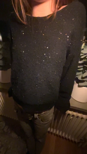 Mörkblå glittrig tröja med öppen rygg - Mörkblå stickad tröja med glittriga detaljer och snygg öppen rygg med band över axlarna. Tröjan har lång ärm och en loose passform, perfekt för dig som gillar att sticka ut med lite extra glitter. Passar till jeans eller kjol för en cool look.