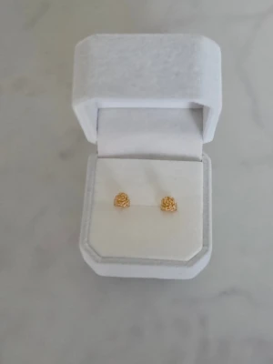Örhängen Rosor - Säljer ett par små, eleganta örhängen med detaljrik rosdesign. Örhängena är i klassisk knoppform och har en glansig finish som ger dem en lyxig känsla. Perfekta för dig som gillar subtila men snygga accessoarer med blommig touch.