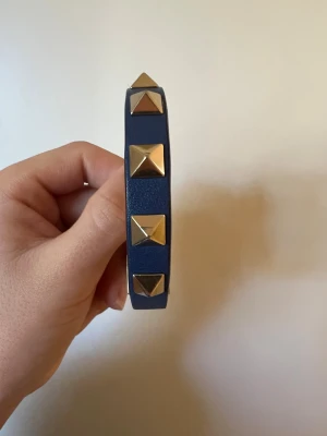 Valentino armband  - Snyggt armband från Valentino Garavani! Marinblått läderarmband med ljust guldfärgade nitar och ett justerbart spänne. Två nitar har varsin liten rispa som syns på första bilden men utöver det är armbandet i toppen skick!🥰