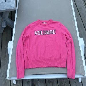 Rosa stickad tröja Zadig & Voltaire - Cool rosa stickad tröja från Zadig & Voltaire med VOLTAIRE-brodyr i vitt och svart framtill. Tröjan har rund hals, långa ärmar och ribbade muddar vid ärmslut och nederkant. Perfekt för dig som gillar färg och statement-plagg.