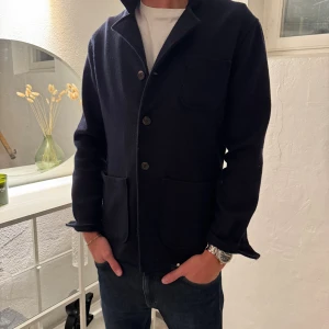 Mörkblå jacka från John Hernric - Snygg mörkblå rock från John Herberg med klassisk krage och tre stora framfickor. Jackan har knappar framtill och är tillverkad i mjuk ull som håller dig varm. Perfekt för dig som gillar stilrena och tidlösa plagg med en chill vibe.