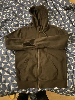 Svart hoodie med dragkedja - Svart hoodie med huva och dragkedja framtill. Tröjan har två fickor på magen och långa ärmar. Klassisk och enkel design, perfekt för chill dagar. Materialet känns mjukt och bekvämt, troligen bomull eller polyester. Passar dig som gillar basic streetwear.