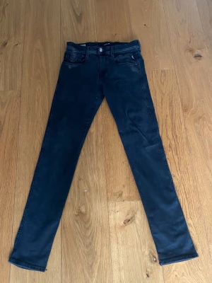Replay Anbass svarta slim jeans - Svarta Replay Anbass jeans i slim fit med klassisk femficksdesign och snygga detaljer på bakfickorna. Jeansen har en smal passform och är tillverkade i stretchigt jeansmaterial för extra komfort. Perfekt för dig som gillar stilrena och moderna jeans.