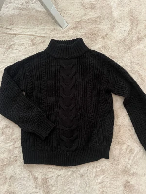Stickad tröja från Vila - Svart stickad tröja från Vila med grovstickat flätmönster framtill och ribbade muddar. Tröjan har hög krage och långärmad passform, perfekt för att hålla värmen. Materialet är stickat och ger en mysig vibe. Storlek S, Knappt använd 