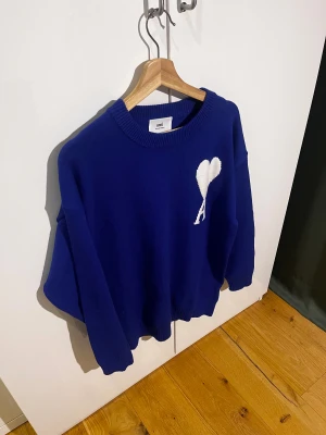 Blå stickad tröja från Ami - Snygg blå stickad tröja från Ami med vit hjärtlogga på bröstet. Tröjan har rund hals, ribbade muddar och en loose passform som ger en chill vibe. Perfekt för dig som gillar stilrena detaljer och vill ha något som sticker ut lite extra. Tags sitter kvar(oanvänd), samt en påse till tröjan:) MVH ItsForfits 🌟