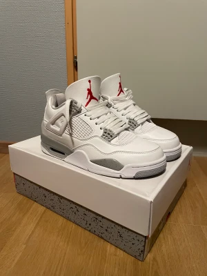 Nike Air Jordan 4 White Oreo - Nike Air Jordan 4 White Oreo med vit ovandel i skinn, grå detaljer med stänkmönster och röda Jumpman-loggor på plösen. Klassisk siluett med meshpaneler, snörning och synlig Air-enhet i sulan. Perfekta sneakers för dig som vill sticka ut med stilrena och ikoniska skor. Använda 2 gånger då ja nu vill sälja dem för att kunna köpa nya till sommaren PRISET KAN ÄVEN DISKUTERAS 