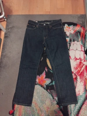 Levi's 511 mörkblå jeans W33 L32 - Säljer ett par Levi's 511 jeans i mörkblå tvätt. Klassisk femficksmodell med orange sömmar och rak passform. Tillverkade i bomull med Water<Less-teknik. Perfekta för dig som gillar stilrena och tidlösa jeans.