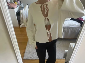 Vit stickad tröja med snörning - Säljer en vit stickad tröja med långa ärmar och öppen front med snörning i tre sektioner. Tröjan har en loose passform och croppad längd, perfekt för dig som gillar trendiga detaljer och vill sticka ut lite extra.
