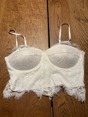 Vit spetskorsett från Amisu, M - Säljer en vit korsett från Amisu i storlek M med justerbara axelband och snygg spets över hela toppen. Korsetten har dragkedja bak och fina spetsdetaljer längs nederkanten. Kuporna är lätt vadderade och insidan är mjuk och slät. Perfekt för dig som gillar romantisk stil.