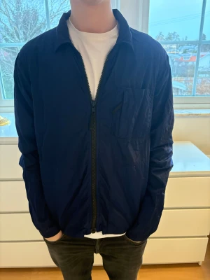 Mörkblå vindjacka Peak Performance - Säljer en mörkblå vindjacka från Peak Performance. Jackan har en clean look med dragkedja framtill, bröstficka och klassisk krage. Tillverkad i lätt polyester som passar perfekt för vår och höst. Enkel och stilren design som funkar till det mesta.