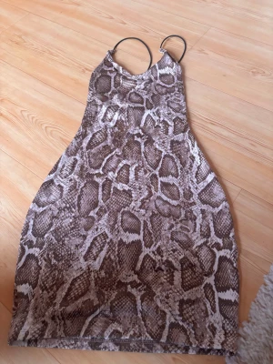 Brun ormmönstrad klänning H&M XS - Säljer en snygg brun och beige klänning från H&M i storlek XS. Klänningen har tunna axelband och ett coolt ormmönster som verkligen sticker ut. Modellen är kort och figurnära, perfekt för dig som gillar att synas. Materialet är mjukt och följsamt polyester.