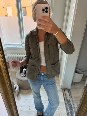 Grön overshirt med fickor - Säljer en grön overshirt med klassisk krage och fyra stora fickor framtill. Jackan har knappar hela vägen och är långärmad. Perfekt att slänga över en t-shirt för en chill och avslappnad look. Materialet känns som bomull och är mjukt mot huden.