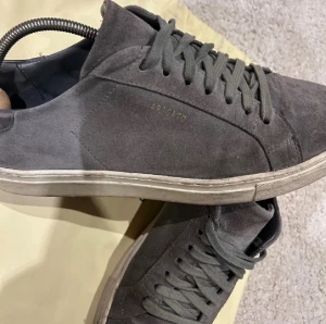 Grå sneakers från Axel Arigato - Snygga grå sneakers från Axel Arigato i mocka med klassisk låg profil och rund tå. Skorna har snörning och en vit platt sula med diskret logga på hälen. Perfekt för dig som gillar stilrena och minimalistiska sneakers med premiumkänsla. Priset går att diskuteras!