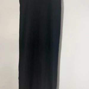 Svart ribbad långkjol - Säljer en svart långkjol med snyggt ribbad struktur. Kjolen har en rak och enkel siluett som ger en clean look. Perfekt för dig som gillar minimalistisk stil och vill ha något som är lätt att matcha med olika toppar.