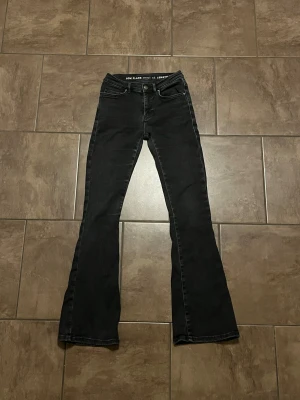 Svarta bootcut jeans low flare XS - Svarta BikBok never denim jeans med låg midja och bootcut/flare-ben. Klassisk femficksmodell med knapp och dragkedja framtill. Snygg passform som sitter tajt upptill och släpper ut vid bensluten. Storlek XS, längd 31, stretchiga och normala i storleken. Lite slitning på ena bakfickan men detta syns knappt. 