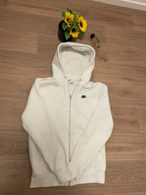 Vit hoodie från Nike med dragkedja - Vit Nike zip-up hoodie i mycket bra skick! En klassisk och bekväm hoodie med Nike-logga på bröstet som passar perfekt för både träning och vardagsbruk. Materialet är mjukt och håller dig varm under kyligare dagar. Storlek och material finns på etiketten. Kontakta mig gärna vid frågor eller intresse. 