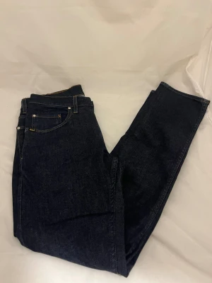 Mörkblå jeans från tiger of sweden - Snygga mörkblå jeans från tiger of sweden  med klassisk femficksdesign och kontrastsömmar. Modellen har raka ben och normal passform, med en läderpatch bak i midjan. Perfekta för dig som gillar stilrena och tidlösa jeans.