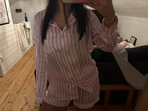 Randiga rosa och vita pyjamas - Säljer ett par söta pyjamas med rosa och vita vertikala ränder. Shortsen har en avslappnad passform och är gjorda i mjuk bomull, perfekta för mysiga hemmakvällar. 