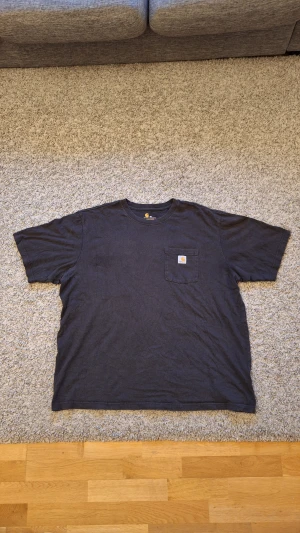 Svart Carhartt t-shirt - Svart t-shirt från Carhartt i storlek XXL, men skulle nog säga den passar mer som XL/L. Original fit. 100% bomull. Använd fåtal ågnger och skicket är jättebra. Den har en ficka på vänstra bröstet med loggan. Snygg och skön. Skick: 8.5/10