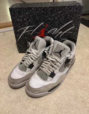 Nike Air Jordan 4 Retro vit/grå - Nike Air Jordan 4 Retro sneakers i vit och grå färg med svarta detaljer. Skorna har snörning, meshpaneler och en platt sula med synlig Air-enhet. Ikonisk Jumpman-logga på plösen och klassisk siluett. Materialet är skinn och syntet med inslag av mocka. Tvättar innan jag skickar !!!