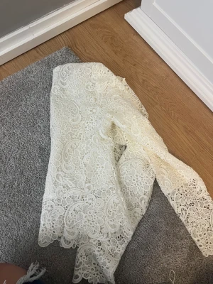 Vit spetsjacka från Amisu - Säljer en vit spetsjacka från Amisu med snygga detaljer och dragkedjor framtill. Jackan har ett unikt spetsmönster över hela ytan och är långärmad. Perfekt för dig som vill sticka ut med en cool och feminin look.