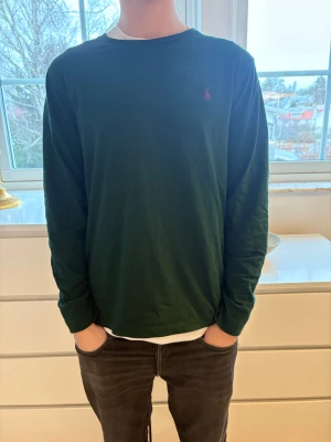 Mörkgrön långärmad tröja Polo Ralph Lauren - Säljer min mörkgröna långärmad tröja från Polo Ralph Lauren med klassisk röd logga broderad på bröstet. Tröjan har en rund hals och är i en slim fit-modell. Tillverkad i mjuk bomull som är skön mot huden, perfekt för dig som gillar stilrena och enkla plagg. Inte använd speciellt mycket.