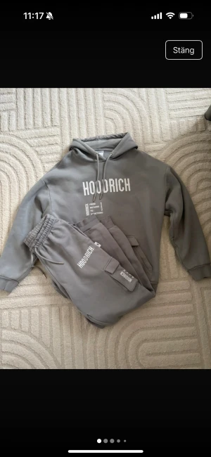 Grå hoodie från Hoodrich med tryck - Snygg grå hoodie från Hoodrich med vit textprint både fram och bak. Tröjan har huva med snörning, magficka och ribbade muddar. Materialet är mjuk bomull och passformen är loose, perfekt för chill dagar. Hoodrich-logga och statement-tryck ger streetkänsla. Är i storlek S och den är ganska stor i storleken 