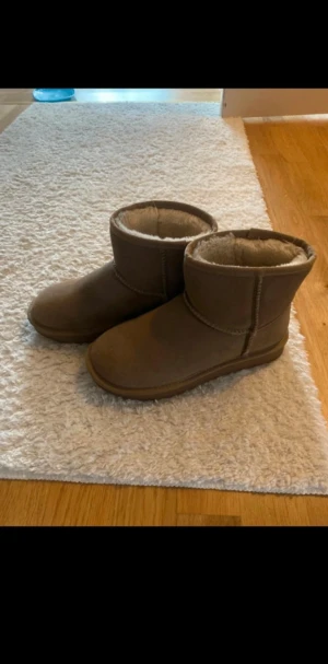 Uggs - Mysiga beiga boots med rund tå och platt sula. Utsidan är i mocka och insidan har ett fluffigt pälsfoder som håller fötterna varma. 