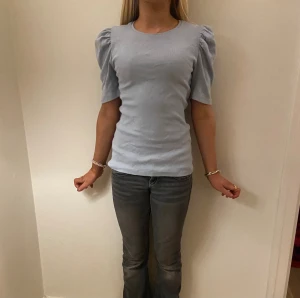 Ljusblå topp med puffärm från Pieces - Supersöt ljusblå topp från Pieces i ribbad bomull. Modellen har korta puffärmar och rund halsringning, vilket ger en trendig och feminin vibe. Perfekt att styla med jeans eller kjol för en fräsch look.