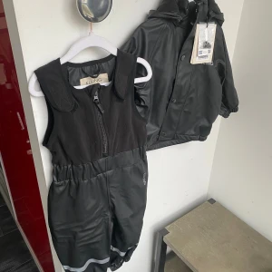 Ottawa Fodrat Regnställ Always Black stl 74/80 - Ottawa Fodrat Regnställ Always Black  Dags att hoppa i vattenpölar. Svart Ottawa regnställ från Kuling. Regnstället har svetsade sömmar.   - Mjukt fleecefoder.  - Jacka med avtagbar huva, dragkedja framtill och resårmuddar.  - Byxor med en överdel i fleece, kardborreband på axlarna, en dragkedja framtill, resår i midjan och slitstarka, justerbara fothällor i silikon.  - Reflexdetaljer för bättre synlighet.  - Vattenavvisande och PFC-fri BIONIC-FINISH®ECO-impregnering.  