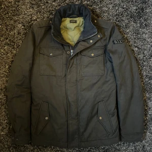 Svart field jacket från Diesel - Parkajacka från Diesel i svart med quiltad grön insida. Jackan har fyra fickor med lock och tryckknappar, hög krage och dragkedja framtill. Diesel-logga på ärmen ger en cool touch. Perfekt för kalla dagar och snygg till streetwear.