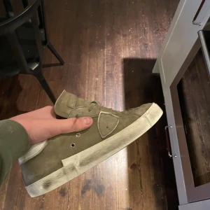 Beige Philippe Model sneakers i mocka - Säljer ett par beige sneakers från Philippe Model Paris med ovandel i mocka och vita detaljer på häl och sula. Skorna har snörning, rund tå och platt sula. Klassisk design med metallöljetter och logotyp på sidan. Perfekta för en chill och stilren look.