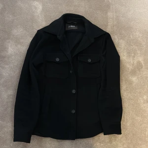 Svart overshirt från Collection - Svart overshirt med klassisk krage och stora bröstfickor med knappar. Jackan har en rak passform, långa ärmar och stängs med knappar framtill. Perfekt att slänga över en hoodie eller t-shirt för en chill look.