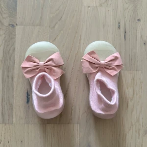 Söta rosa ballerinaskor med rosett skor  - Supergulliga ballerinaskor i ljusrosa med stor rosett framtill. Skorna har en mjuk stickad ovandel och en platt, flexibel sula i syntet som ger bra grepp. Perfekta för dig som gillar en söt och feminin stil. Passar små fötter och är lätta att ta på.Ett par söta, rosa babyskor med rosetter. För cirka 1 år + 