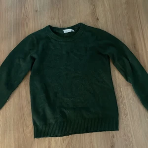 Mörkgrön stickad tröja från Vila - Mysig mörkgrön stickad tröja från Vila med rund halsringning och ribbade muddar vid ärmslut och nederkant. Knappt använd och perfekt till vintern. Skriv om ni har några frågor💕