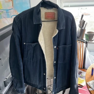 Vintage teddyjacka från Levi's -  mörkblå teddyjacka från Levi's i L. Jackan har två stora bröstfickor, klassisk krage och är fodrad med mjuk teddy på insidan. Yttermaterialet är manchester och jackan stängs med knappar 